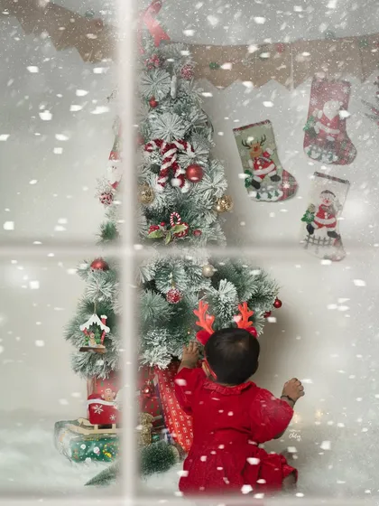 A little one decorating the Christmas tree. This creative shot, framed as if looking through a snowy window, captures the wonder and excitement of the holiday season.
