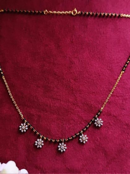 A very delicate 92.5 silver gold-plated mangalsutra with five small floral charms made of American diamonds. It's a subtle and beautiful piece for daily wear.