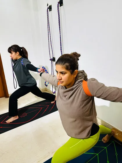 Two students practice a variation of Warrior Pose. We have classes from Monday to Friday, with both morning and evening sessions available to fit your schedule.