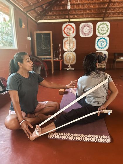 Using a yoga strap is a wonderful way to make challenging poses more accessible. Here, Neelam guides a student in a seated forward bend, demonstrating how props can help maintain alignment and deepen a stretch safely. We teach you to be a resourceful and inclusive instructor.