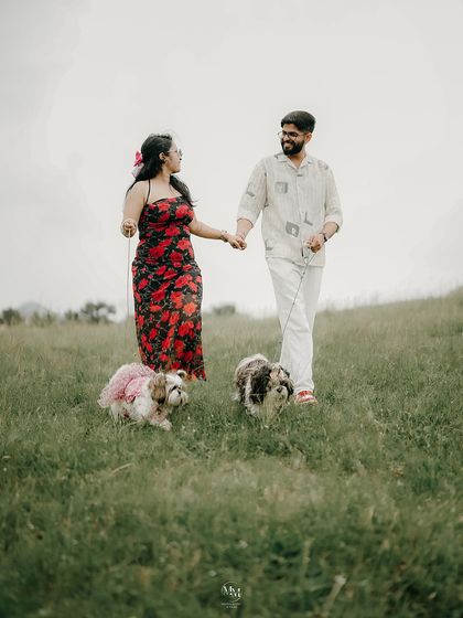 Hand in hand, paw in paw. A lovely shot of the couple walking their two adorable dogs in a lush green field, a perfect family portrait.