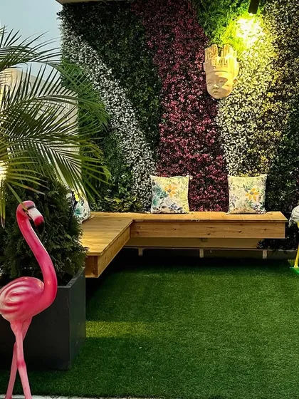 A vibrant terrace corner in Noida, featuring a colorful vertical garden as a backdrop for a cozy wooden bench. The pink flamingo adds a playful touch.