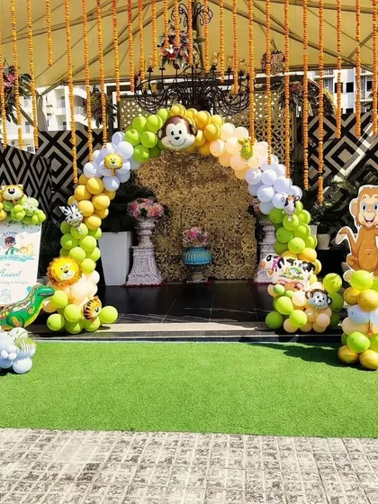 An outdoor jungle theme entrance arch for a party. The setup includes a lush green turf floor, a balloon arch with monkey characters, and hanging floral decorations.