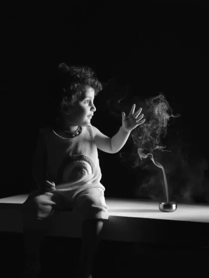 A child’s curiosity is a magical thing. This dramatic black and white studio portrait captures a moment of pure wonder as a toddler interacts with a wisp of smoke. The high contrast and focused lighting create an artistic and memorable image that highlights a child's fascination with the world.