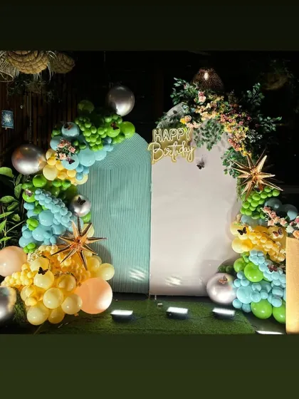 A birthday backdrop with two panels and an organic balloon garland in shades of green, yellow, and blue.
