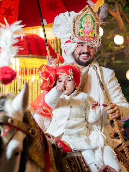 A heartwarming shot of the groom on the horse during his baraat, with a young child in front of him. It's a moment of family, tradition, and joy.
