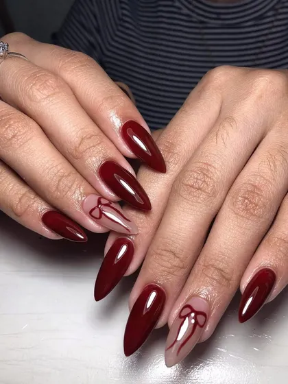 A dramatic, long stiletto set in deep red with delicate bow line art on accent nails. This is a perfect blend of bold color and feminine detail.