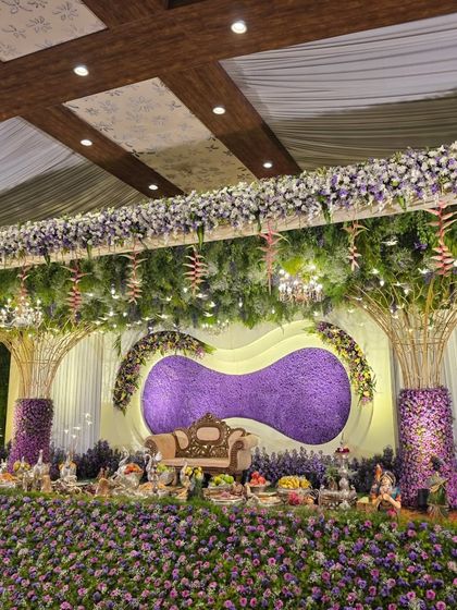 A wider perspective of the purple floral stage, showcasing the elegant white drapery and the ceiling covered in lush greenery and hanging lights. This design is perfect for a glamorous reception or engagement.