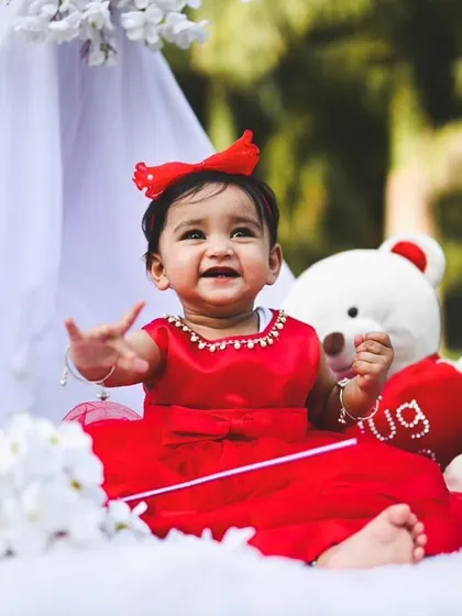 A close-up of the birthday girl in a bright red dress, part of our outdoor teepee setup. The white blanket and props create a clean, bright space that makes the subject pop.