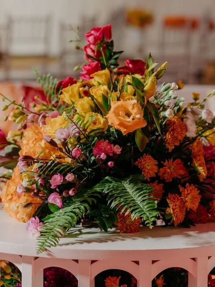 Another angle of the beautiful floral arrangement on the white slatted table, showcasing the mix of ferns, roses, and other colorful blooms.