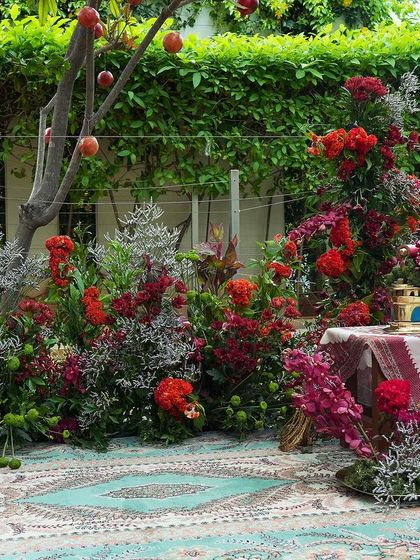 A beautiful photo corner from 'दाड़म ka Bageecha', with a lush floral arrangement on a traditional carpet, set against a tree adorned with pomegranates.