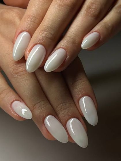 A beautiful milky white manicure on oval-shaped nails. The color is semi-sheer, giving it a soft and natural-looking finish.