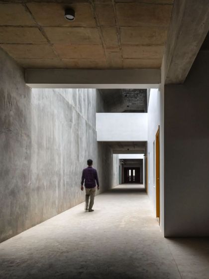 A corridor within MSAP, where the rawness of exposed concrete walls is softened by natural light from above. The space is designed to be a quiet, contemplative passage between the bustling studios.