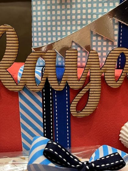 It's all about the details that matter most. This close-up shows a personalized wooden name cutout, "Rayan," on a beautifully wrapped gift from a nautical-themed baby trousseau.