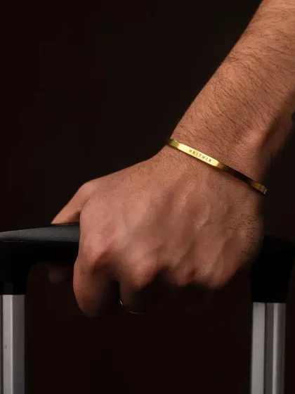 A man holding a suitcase handle, wearing a gold cuff bracelet. This shot positions the bracelet as a perfect travel companion and stylish accessory on the go.