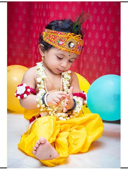 A candid moment during a Krishna-themed shoot, where the child is naturally playing with the flower garland prop.