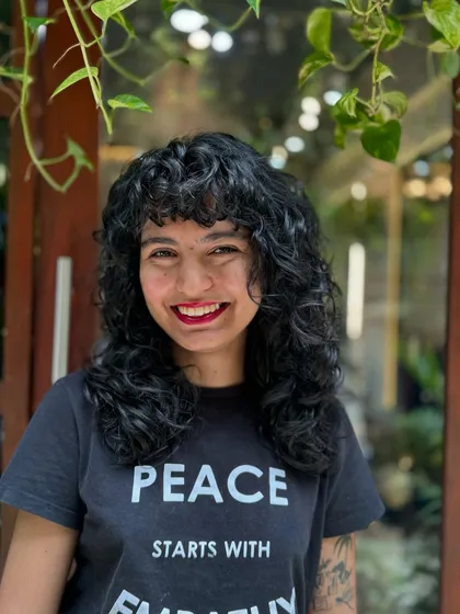 Curly bangs are the cutest! This client is radiating joy with her new fringe and layered cut that perfectly frames her smiling face.