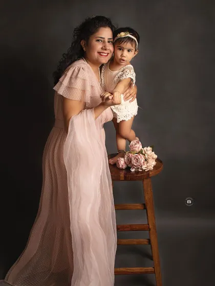 A playful and loving moment between a mother and her daughter. Her daughter standing on the stool adds a fun and dynamic element to the portrait.