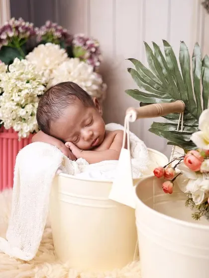 A newborn sleeping in a bucket, surrounded by a beautiful arrangement of flowers. This setup combines rustic charm with floral elegance.