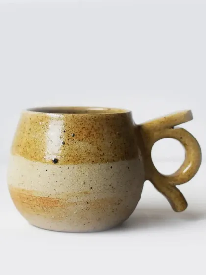 This mug features a unique, sculptural handle and a beautiful two-tone glaze. The rustic, sandy texture makes it a pleasure to hold.
