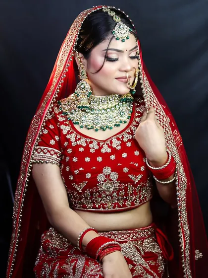 A beautiful side profile of a bride in a classic red lehenga. The focus here is on the harmony between the rich green jewelry and the warm tones of the makeup, demonstrating an understanding of color theory in bridal styling.