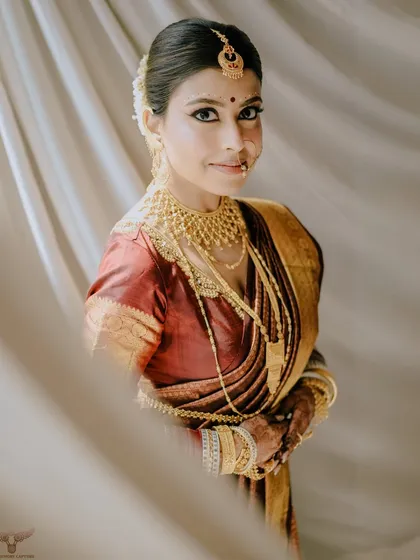 This portrait of a traditional Bengali bride is a study in elegance. The soft, diffused light and the sheer curtain create a dreamy effect, perfectly complementing her golden jewelry and red saree.