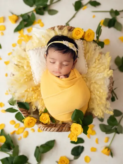 A top-down view of the peaceful newborn in her basket of yellow roses, a perfect composition for a birth announcement or nursery art.