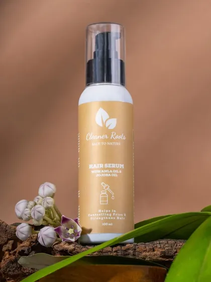 A close-up of Cleaner Roots' Hair Serum, styled with wood and delicate flowers. This highlights the product's natural ingredients and gentle formulation.