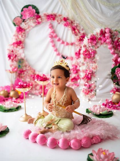 This little one is all smiles in his beautiful Krishna costume, sitting amidst a sea of pink flowers.