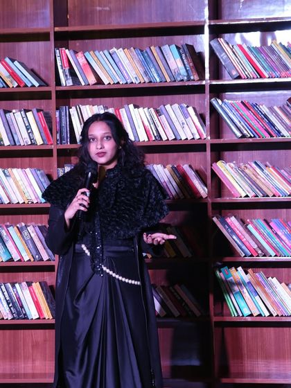 A poet dressed elegantly for her performance, standing against a literary backdrop. Our showcases are professional productions, from the performers to the stage setup.