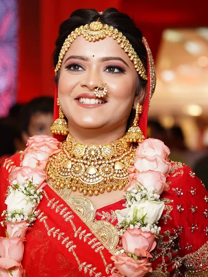 A smiling bride looking radiant. Her look features a classic gold choker and matching jhumkas, paired with a floral garland.