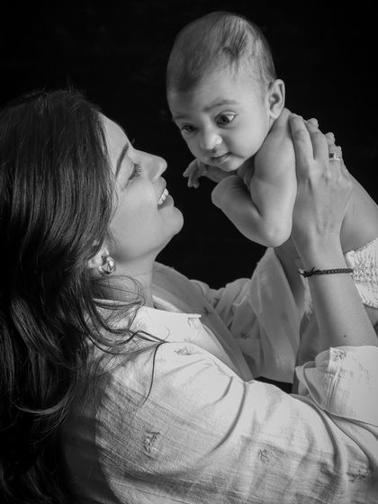 A joyful black and white shot of a mother lifting her baby. The baby's wide-eyed expression and the mother's smile create a dynamic and heartwarming image.