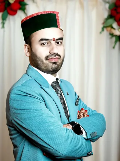A confident groom with arms crossed, wearing his Himachali cap with pride. The formal backdrop complements his sharp, celebratory look.
