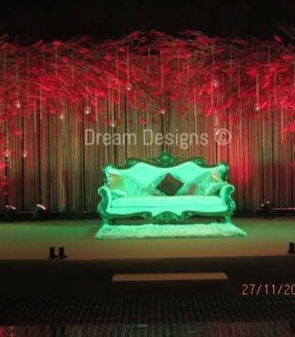 This stage design uses dramatic lighting to create a captivating effect. The backdrop of red branches and a simple, elegant sofa is illuminated with different colored lights to create a dynamic and modern feel for the celebration.
