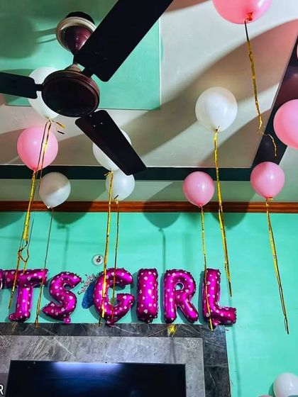 An "It's a Girl" foil balloon sign with simple pink and white balloons floating on the ceiling. This is a great example of a simple yet beautiful way to decorate a room for a baby's homecoming.