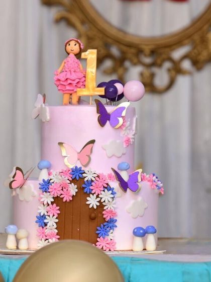 A lovely two-tiered fairy house cake decorated with butterflies and flowers. This design is perfect for a first birthday, creating a whimsical and sweet centerpiece.