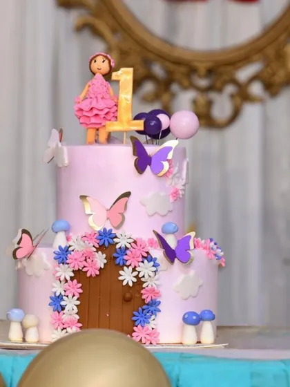 A charming two-tiered fairy house cake, complete with a tiny door, mushrooms, and beautiful flowers. A fondant fairy and butterflies complete this magical scene.