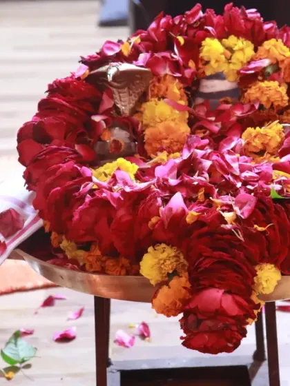 A Shiva Lingam adorned with a garland of fresh red roses and marigolds, prepared as a central part of our worship.