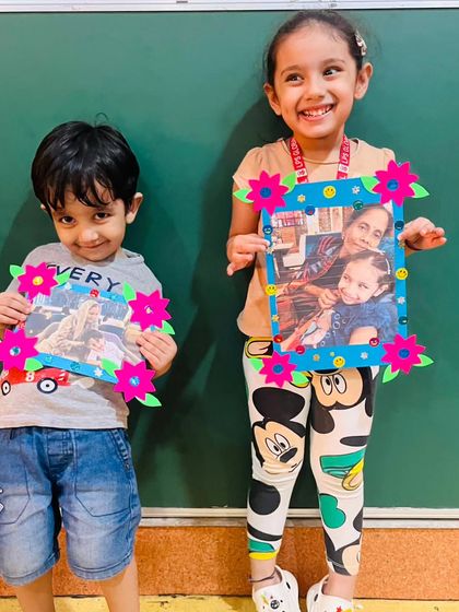 Siblings smile as they hold up the photo frames they crafted for their grandparents. We encourage activities that reinforce family values and the importance of intergenerational relationships.