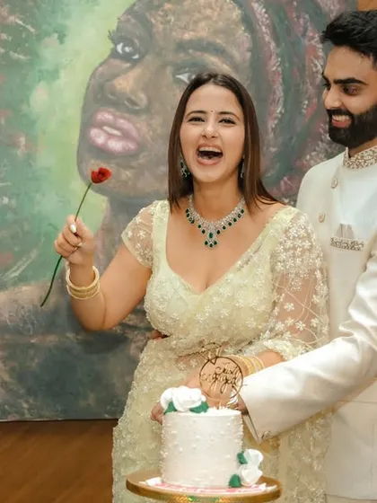 A joyous cake-cutting moment during an indoor engagement celebration in Pune. The couple's happiness is the focus, framed by modern decor and a beautiful piece of art, capturing the celebratory spirit of the occasion.