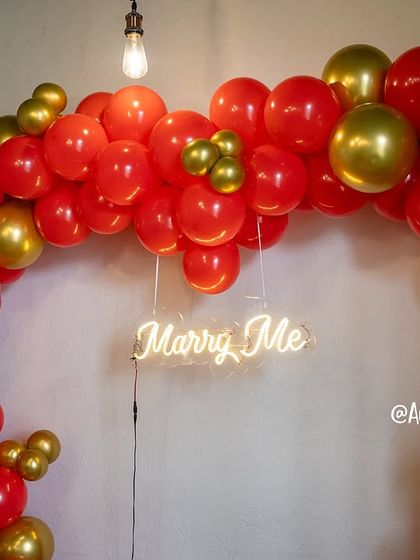 A close-up of the 'Marry Me' neon sign nestled within the vibrant red and gold balloons, adding a modern and heartfelt touch.