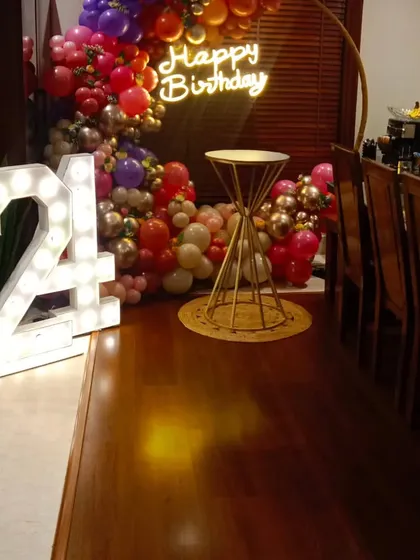 A colorful and chic setup for a 24th birthday. This corner decoration features a balloon arch, a 'Happy Birthday' neon sign, and large marquee numbers, perfect for a house party.