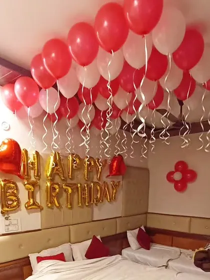 A simple yet classic birthday decoration with red and white balloons on the ceiling, 'Happy Birthday' foil letters, and a few heart-shaped balloons.