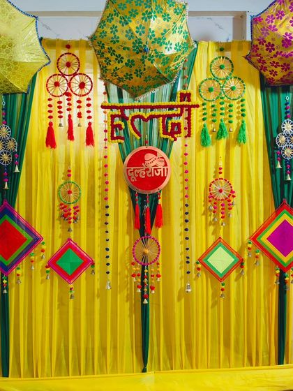 A full view of the 'Dulheraja' Haldi backdrop, featuring bright yellow drapes, decorative umbrellas, and colourful thread-work hangings.