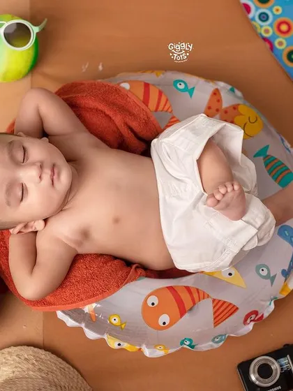 Too hot, but still cool. A baby relaxes on a mini beach chair, enjoying a nap with a coconut drink by his side.