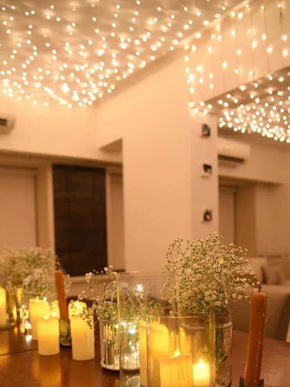 The interplay of the warm fairy lights on the ceiling and the flickering candles on the table creates layers of light, making the space feel incredibly intimate and special.