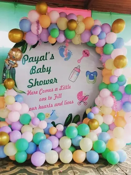 A pastel-themed baby shower decoration for Payal. The custom backdrop is surrounded by a full arch of pastel rainbow balloons, creating a soft and dreamy look for the celebration.