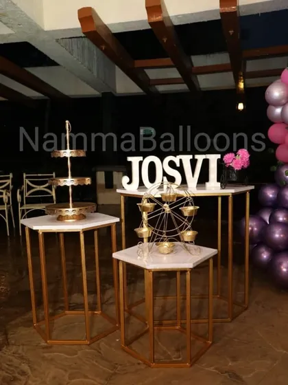 I provide elegant dessert tables and props to match your party's theme. This setup includes hexagonal stands and a miniature Ferris wheel for holding sweets, all in a coordinated gold and white color scheme.