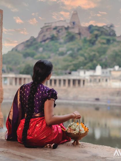 Gazing at the temple on the hill, our model's traditional braid and red and purple saree create a timeless and evocative image.