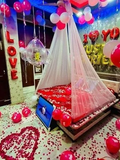 A 'Just Married' first night decoration. The room is filled with red and white balloons, a sheer canopy with lights, 'LOVE' and 'I Love You' foil balloons, and a heart made of rose petals on the floor.